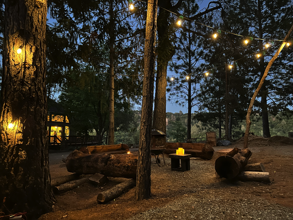 Outdoor log benches with strings lights and a fireplace in the center